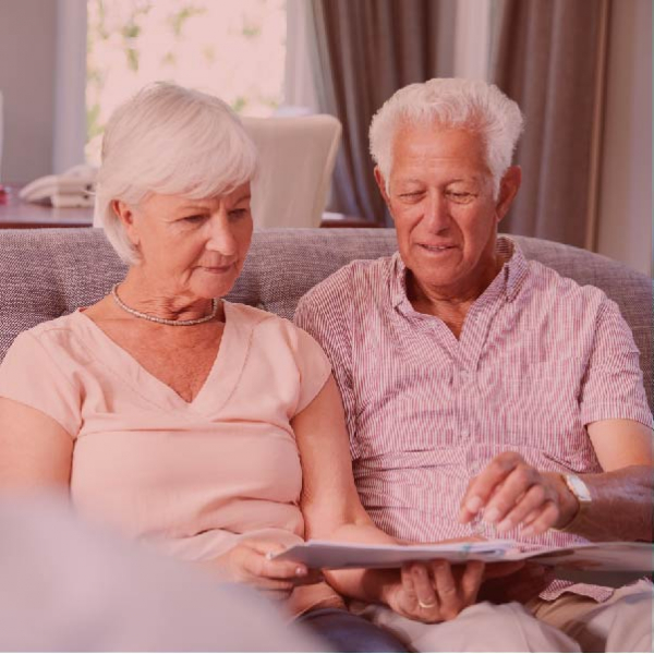 Elderly couple sitting on a couch looking at papers.